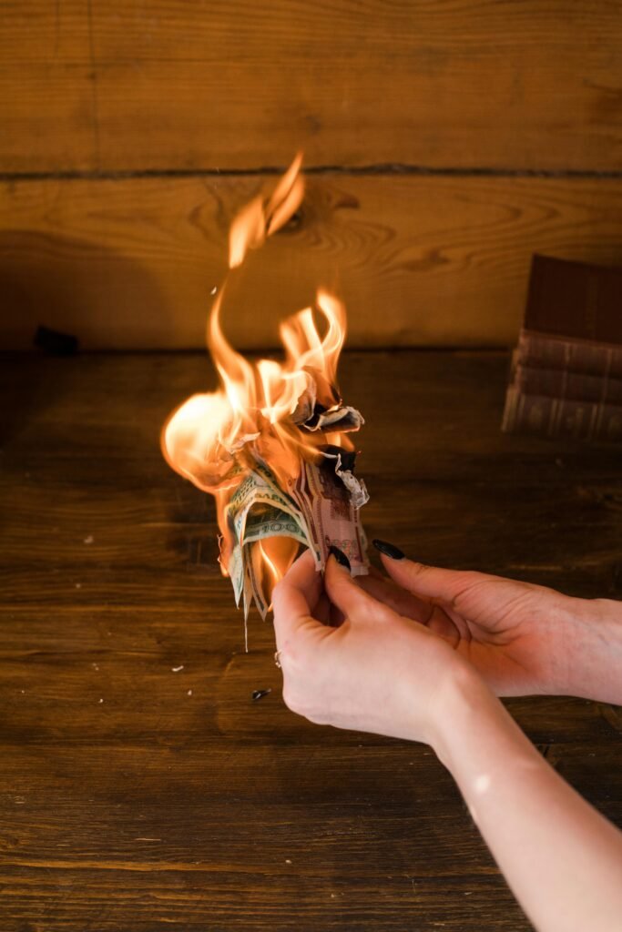 pexels-photo-4588670-4588670 Hands holding burning banknotes against a wooden background, symbolizing financial waste.