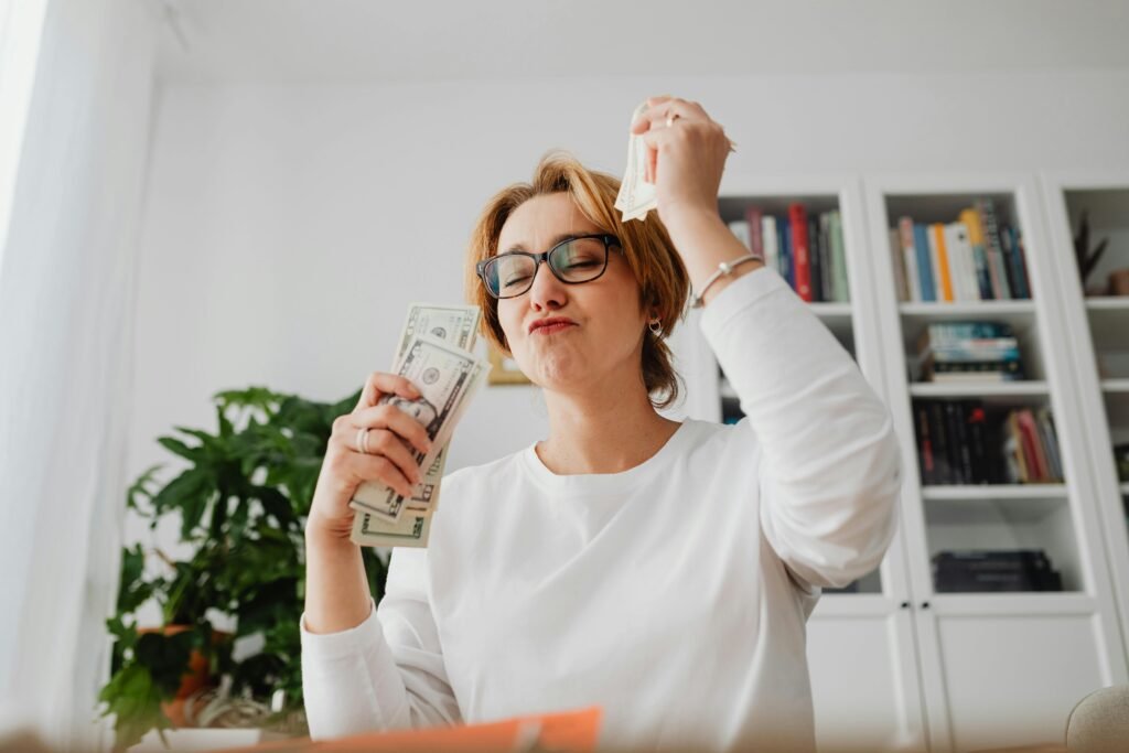 pexels-photo-5900254-5900254 Caucasian woman with glasses holding dollar bills and celebrating indoors.