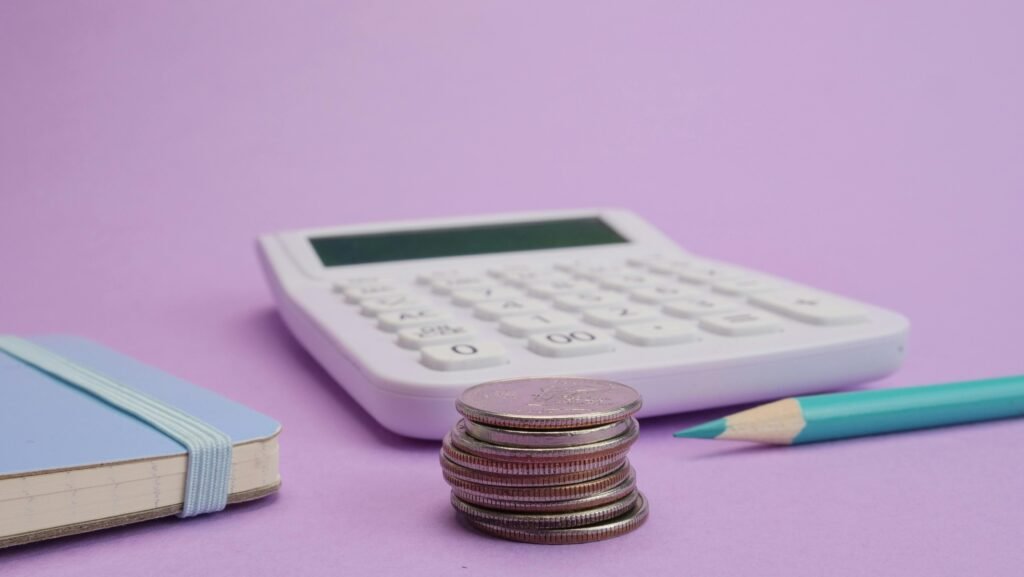 pexels-photo-7054801-7054801 Calculator, coins, and stationery symbolize budgeting and finance on a pastel purple backdrop.