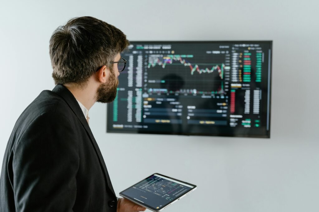 pexels-photo-7567595-7567595 A businessman examines stock market data displayed on a monitor, holding a tablet.